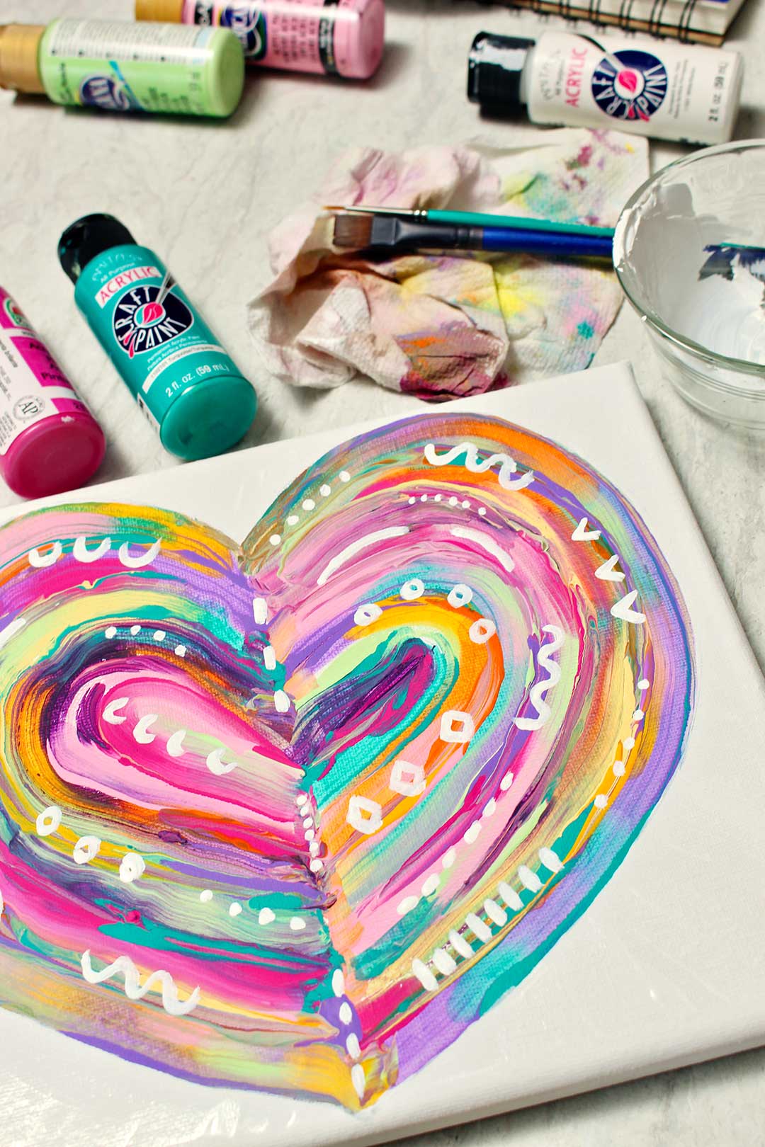 Finished abstract heart painting with white abstract designs with painting supplies near by.