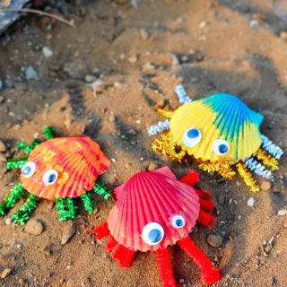 Three colorfully painted seashell crabs on a sandy surface.