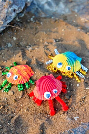 Three colorfully painted seashell crabs on a sandy surface.