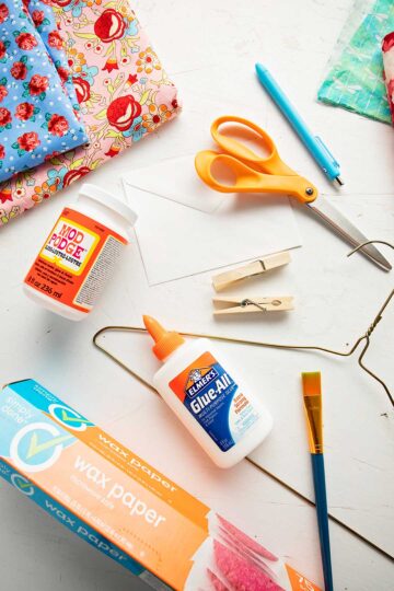 Supplies to make fabric envelopes. Floral fabric, scissors, Elmers glue, Mod Podge, wax paper and a hanger.