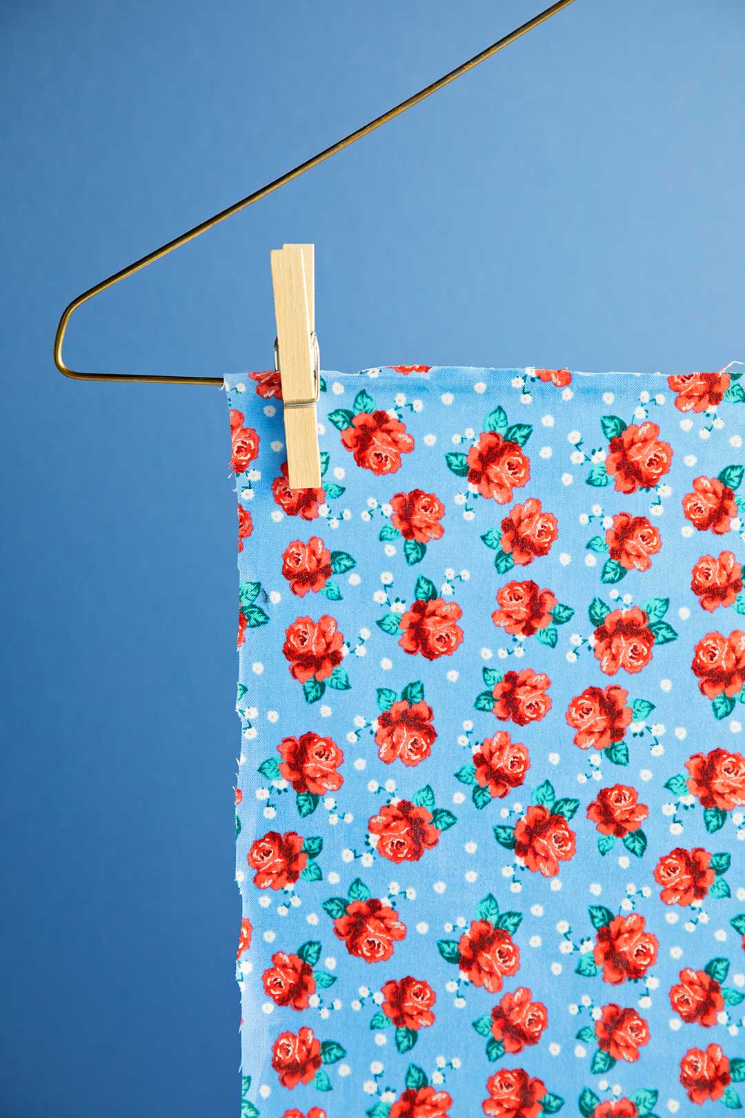 Blue floral fabric hanging to dry, clipped on a hanger against a blue background.
