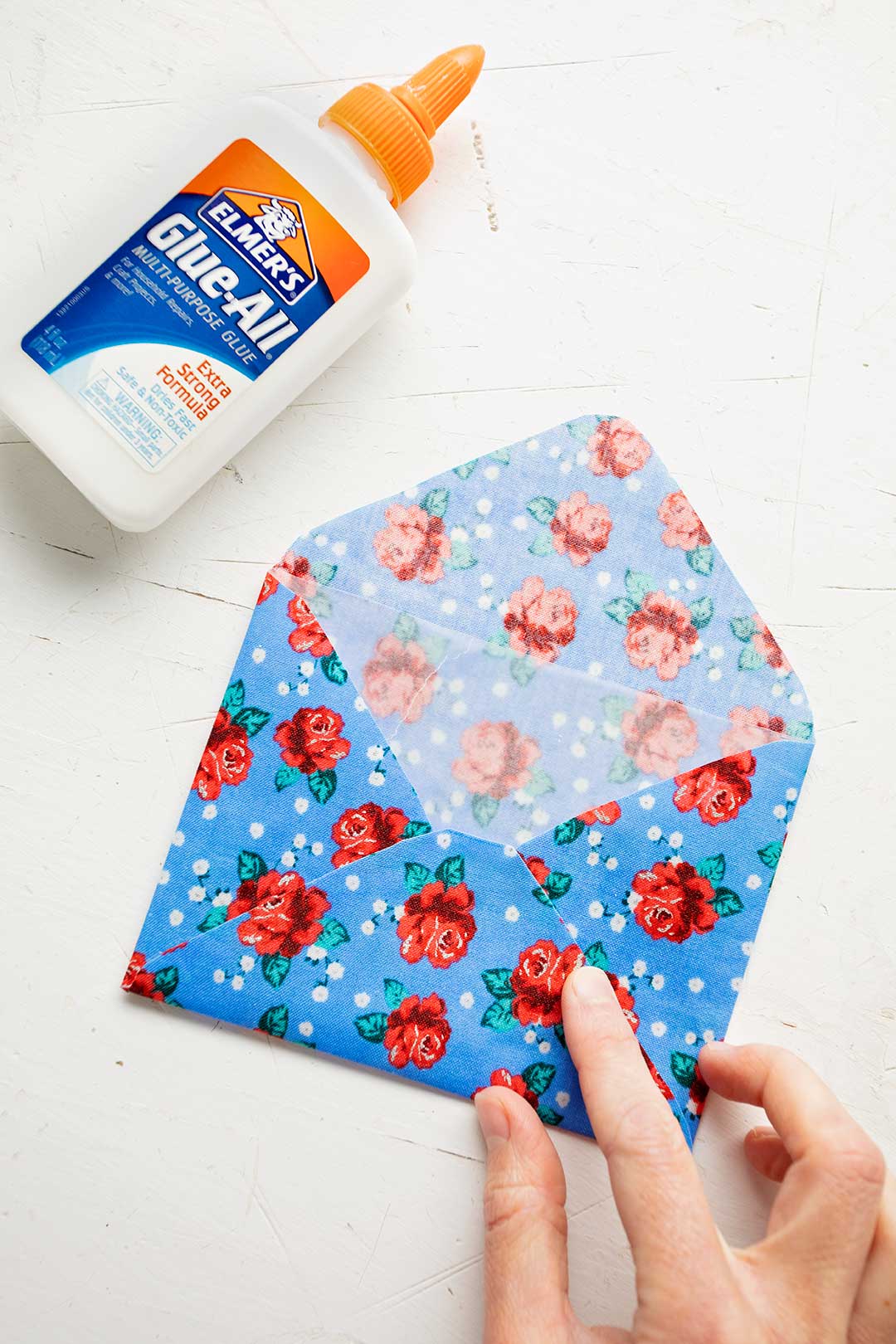 Blue floral fabric envelope opened with a bottle of Elmers glue on white background.