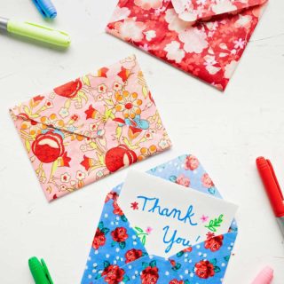 Three colorful floral fabric envelopes with five colored markers on white background.