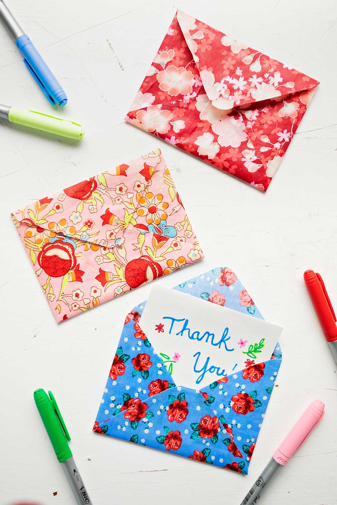 Three colorful floral fabric envelopes with five colored markers on white background.