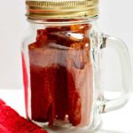 Mason jar of finished fruit leathers with red dish towel resting on white counter top.