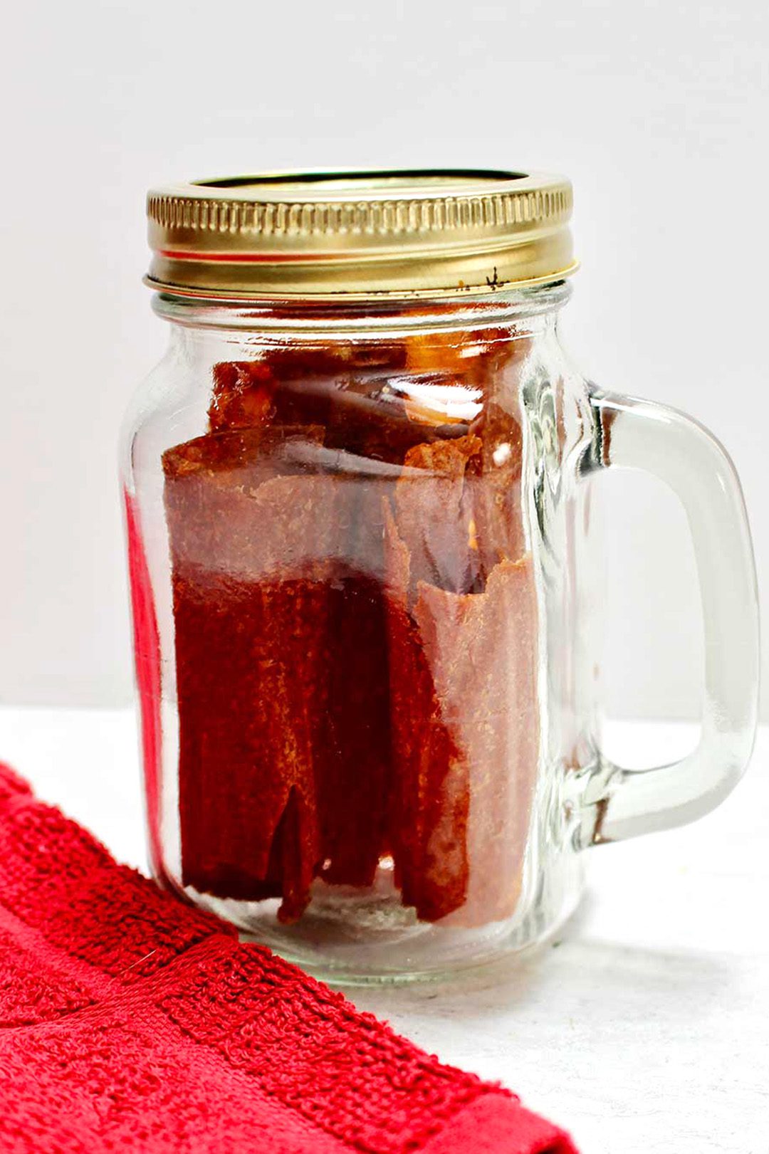 Mason jar of finished fruit leathers with red dish towel resting on white counter top.