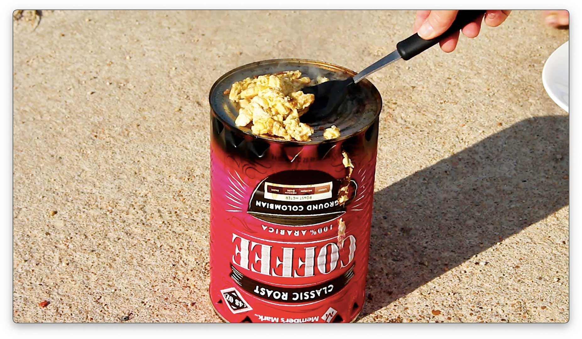 Someone cooking scrambled eggs on coffee can hobo stove.