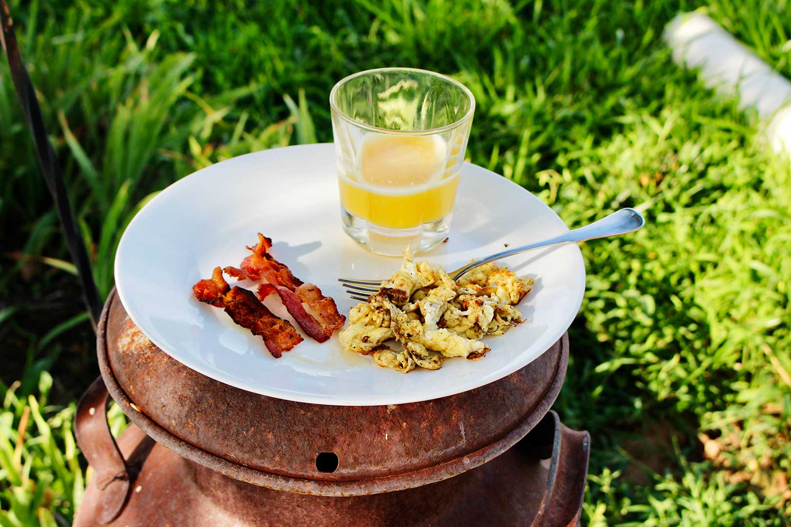 A plate of bacon, eggs and juice breakfast sitting on top of old oil can.