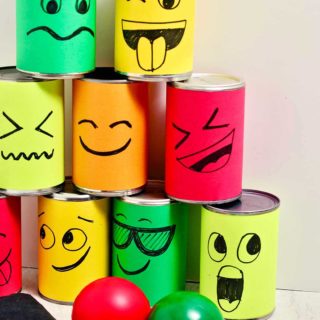 Stacked silly face tin cans in a pyramid shape with a red and green ball and a bean bag.