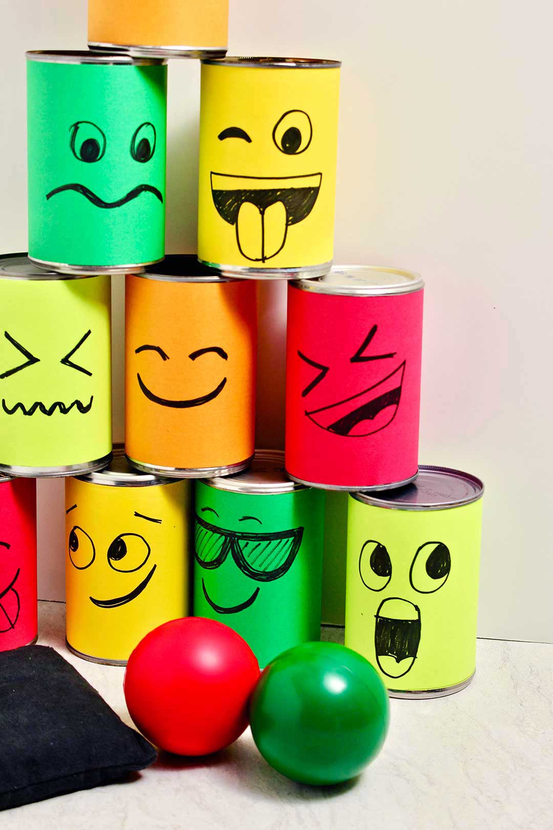Stacked silly face tin cans in a pyramid shape with a red and green ball and a bean bag.