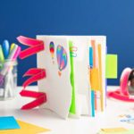 Completed paper bag book decorated with stickers and ribbons with various colorful supplies nearby.