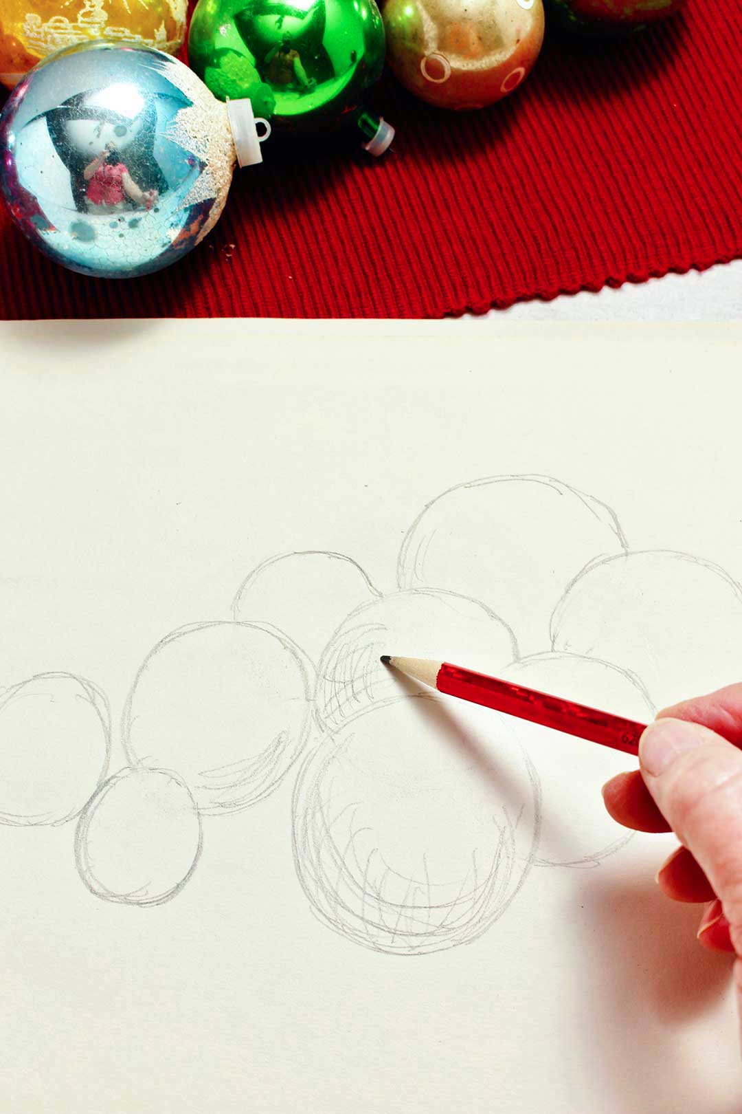 Close up view of person doing rough shedding on sketch of Christmas ornaments.