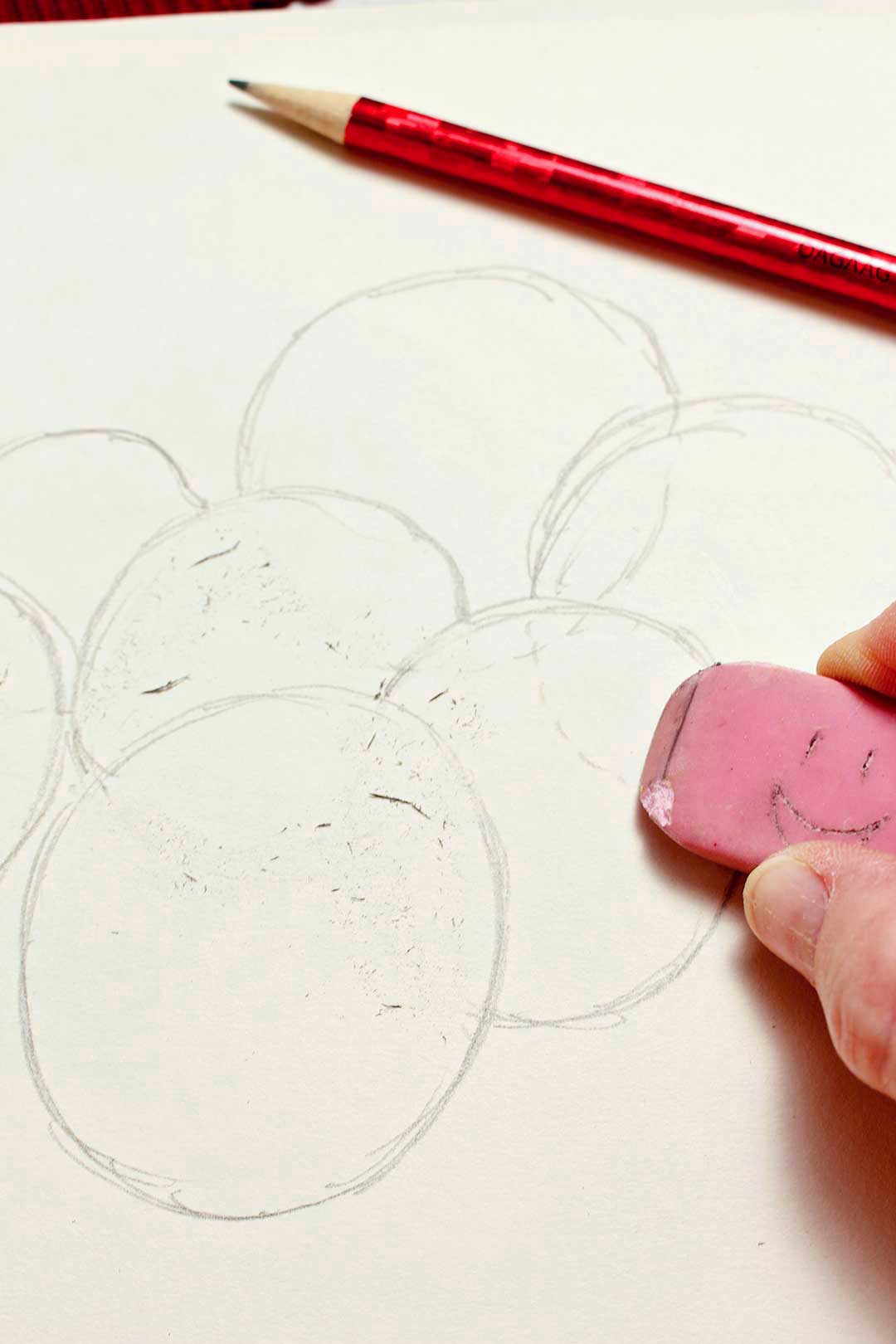Close up view of a person erasing overlapping lines on their sphere drawing with a pink eraser.