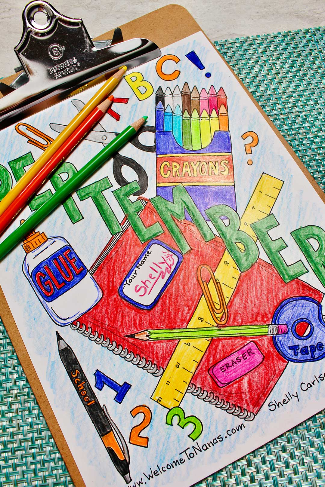 A completed September coloring sheet, decorated with school supplies, clipped into a clip board with colored pencils resting on it.