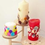 Three pillar candles decorated with buttons resting on wooden stands.