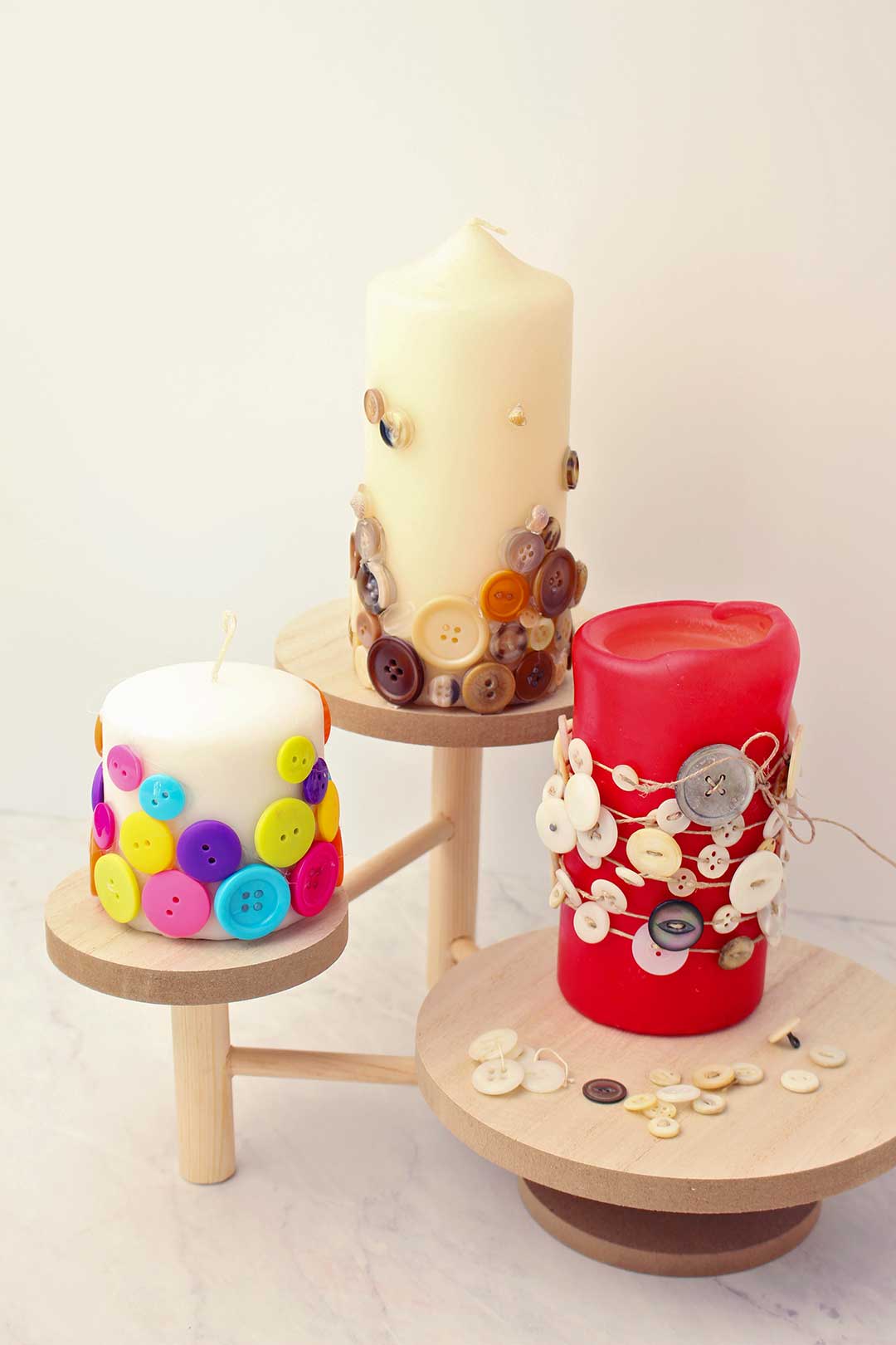Three pillar candles decorated with buttons resting on wooden stands.