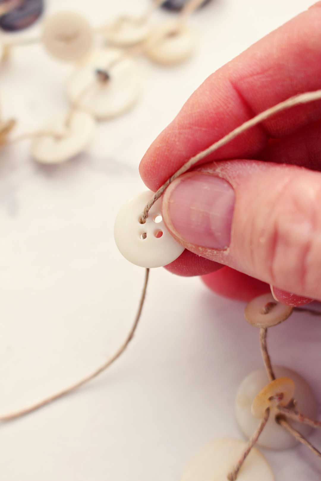 Hand stringing white button on a piece of string.