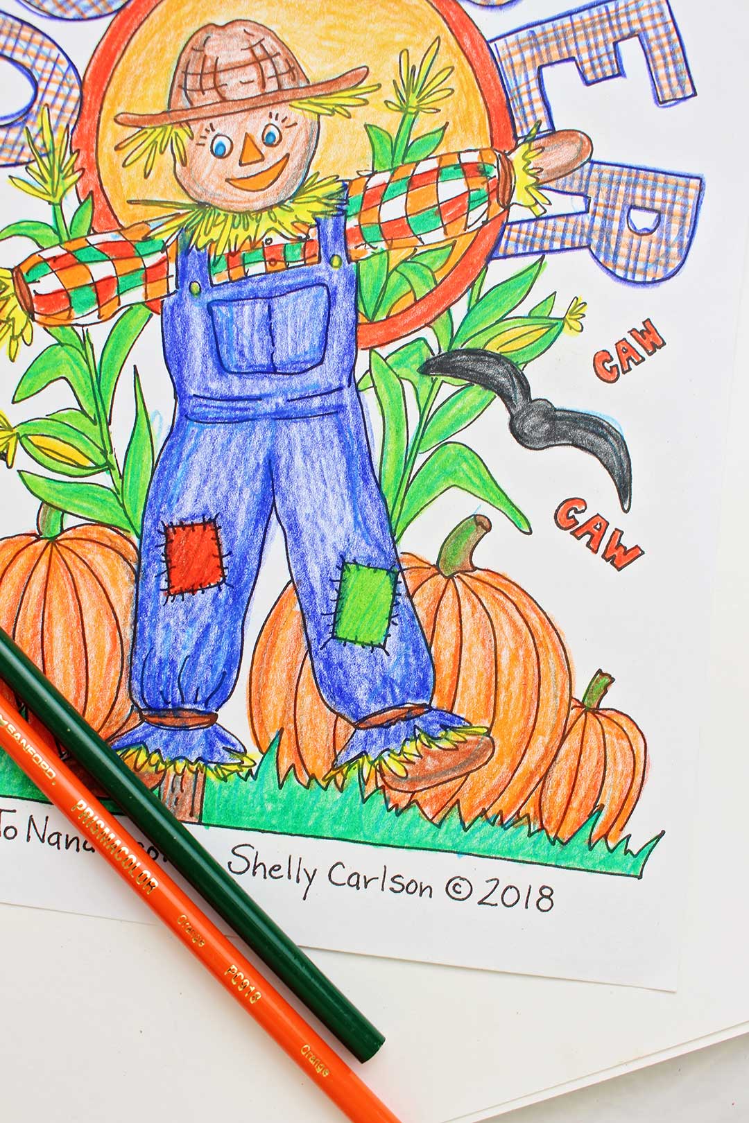 Colored scarecrow coloring page with green and orange color pencil resting on top of it.
