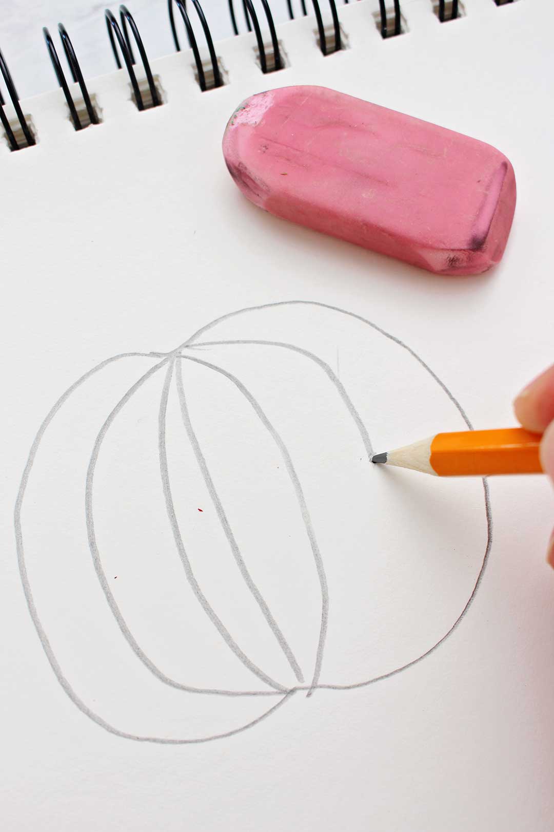 Pencil drawing of the first steps of a pumpkin sketch with pink eraser near by.