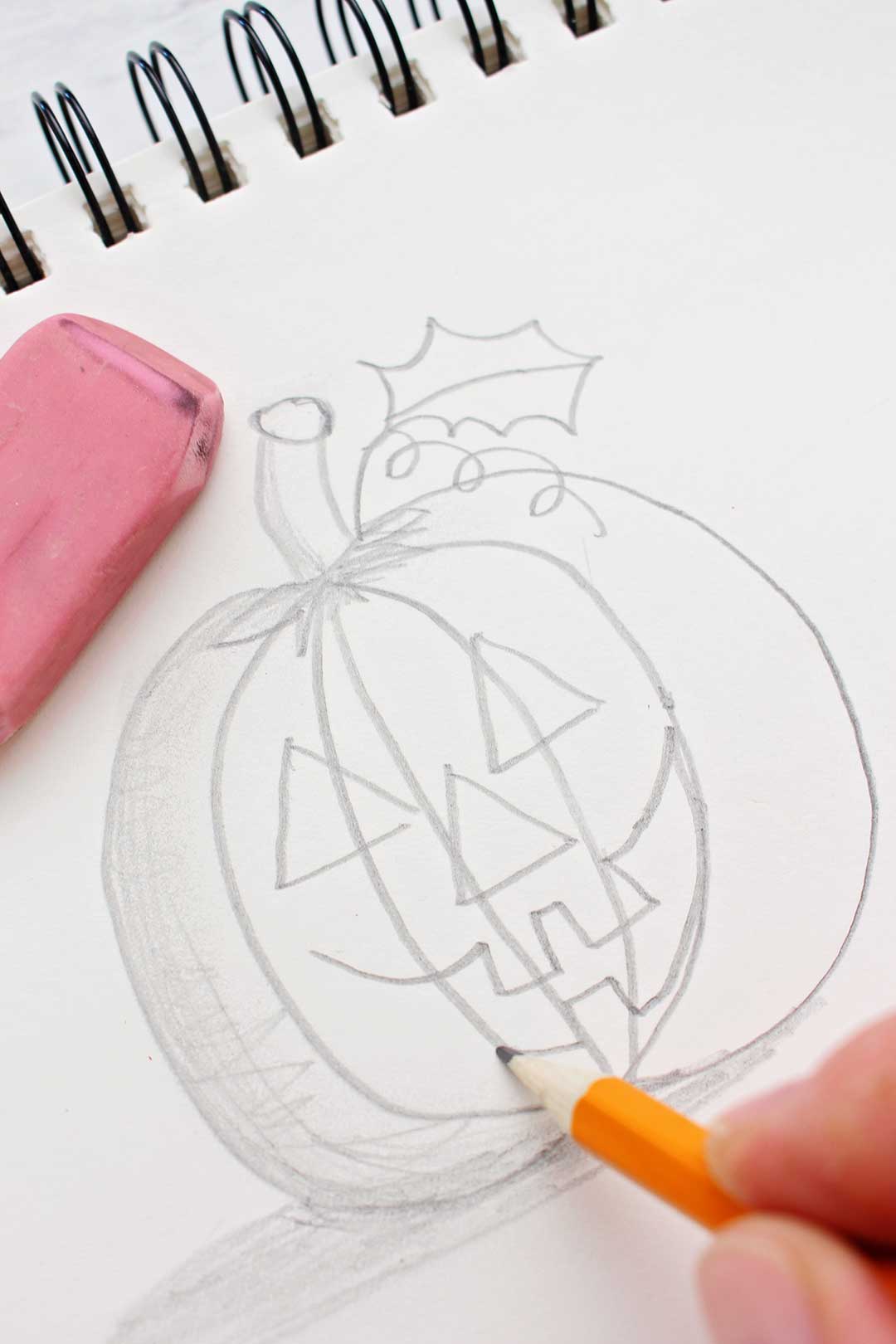 Hand holding pencil drawing the mouth of a jack-o-lantern sketch.