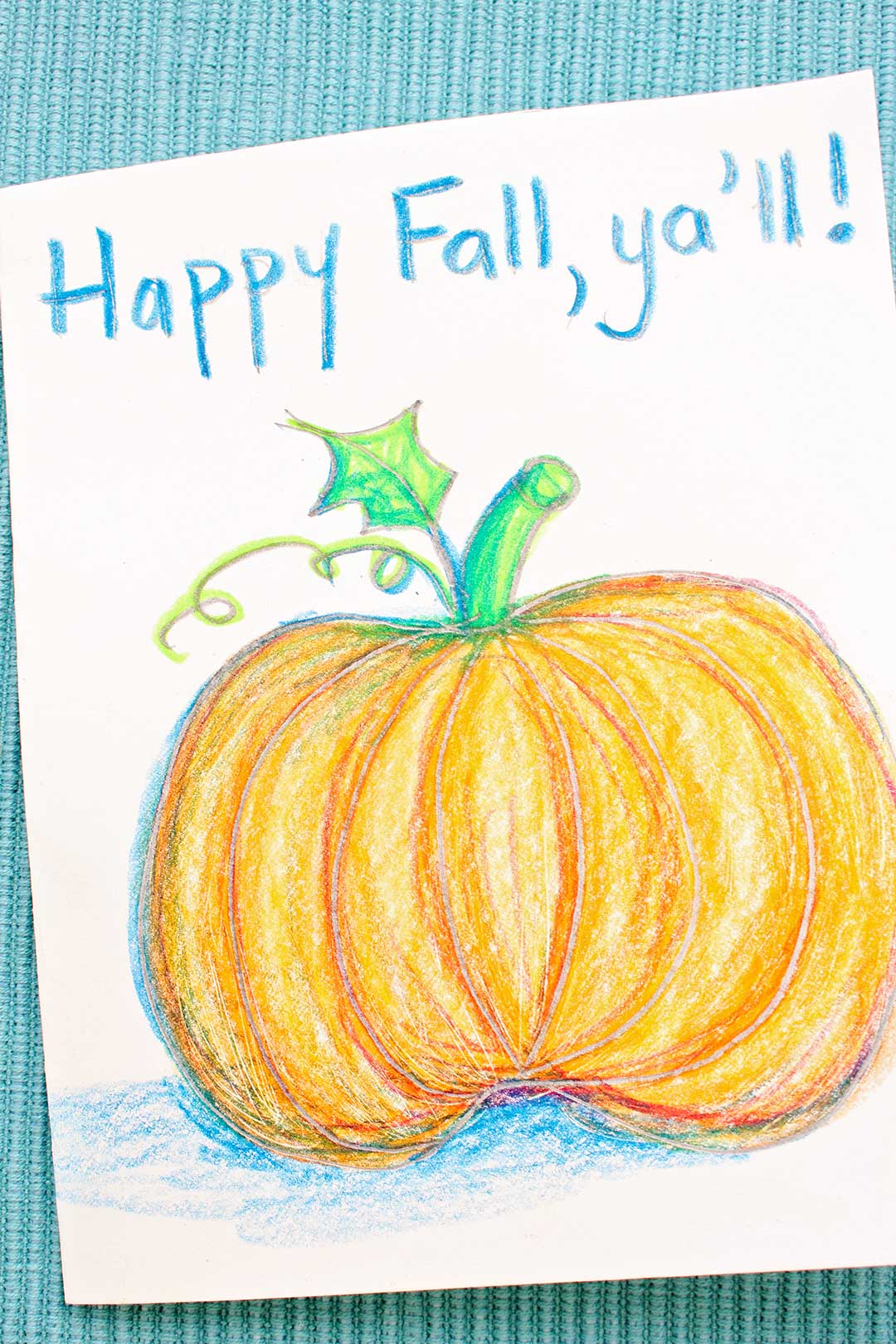 Colored pumpkin sketch greeting card resting on a blue woven placemat.