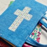 Two completed fabric book covers, one with colorful patchwork fabric and another with denim and a fabric cross.