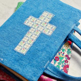 Two completed fabric book covers, one with colorful patchwork fabric and another with denim and a fabric cross.