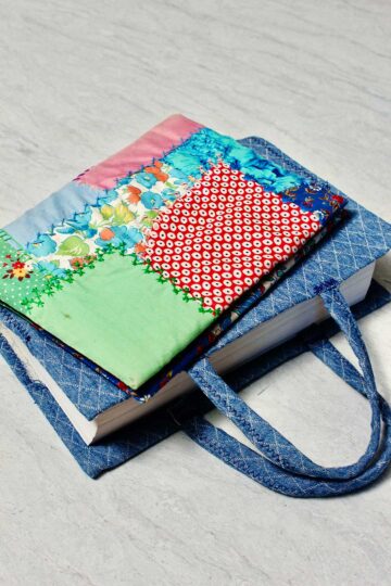 Two completed fabric book covers. One with a colorful patchwork pattern and one with denim fabric.