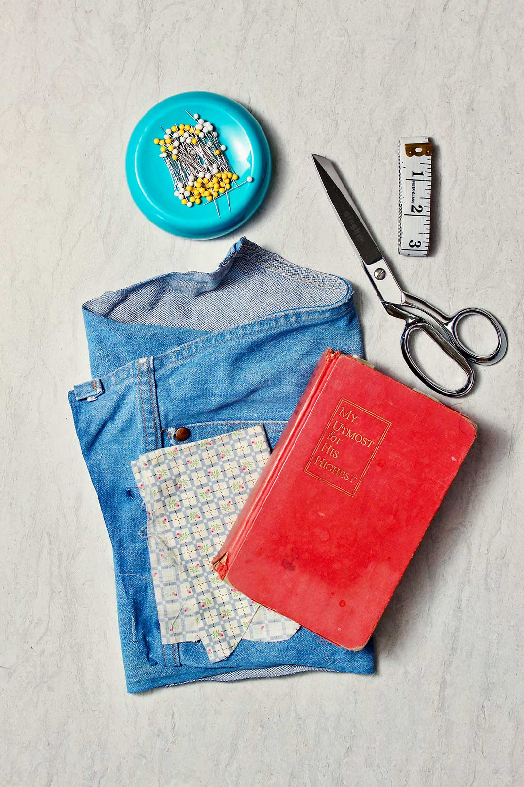 Supplies you will need to make a fabric book cover. Old denim pants scraps, a book, pins, scissors, and a measuring tape.