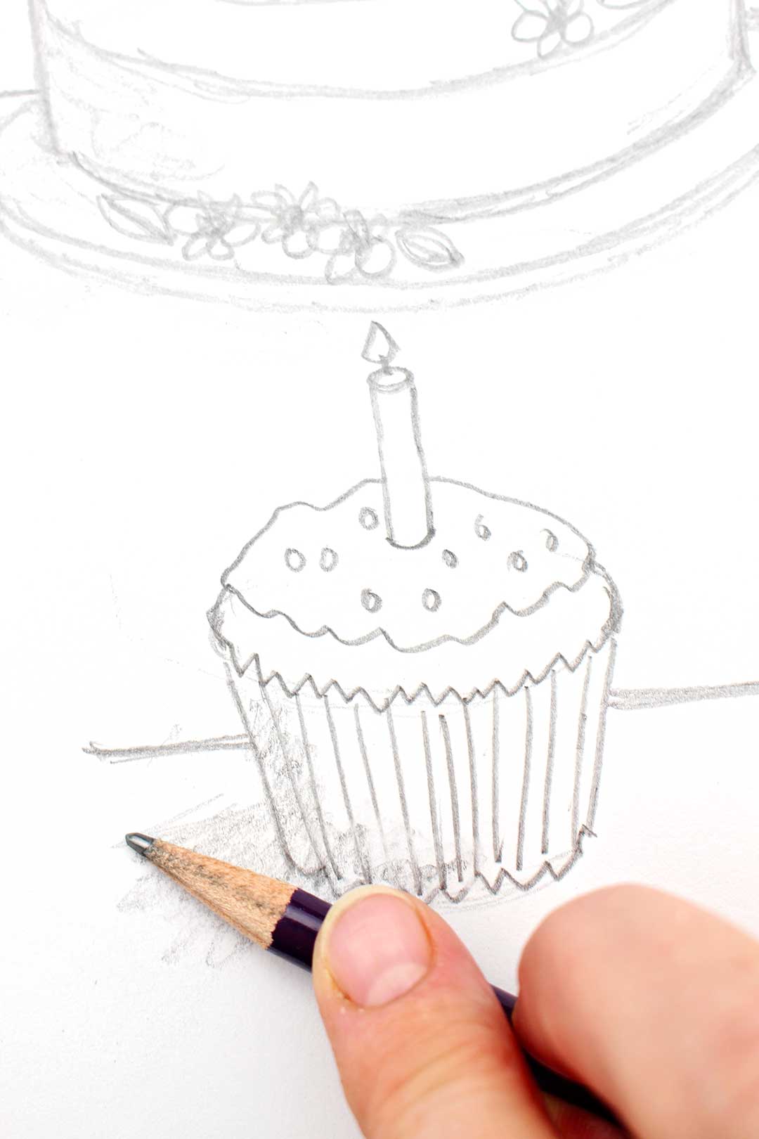 Hand shading a pencil sketch of a cupcake, iced with a candle on top.