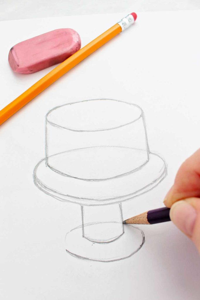 Hand drawing cake stand with a pencil for the layer cake drawing with a yellow pencil and pink eraser near.