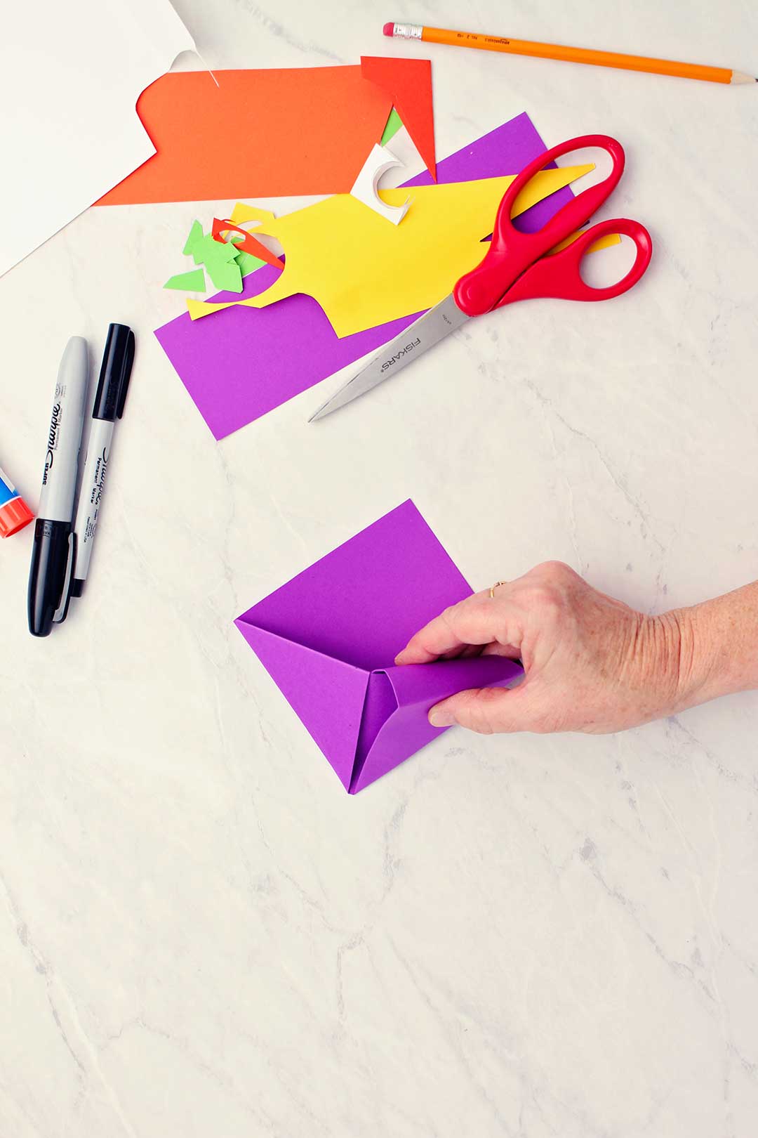 Hand folding in one of the triangle flaps of the purple paper to secure them inside the diagonal center fold.
