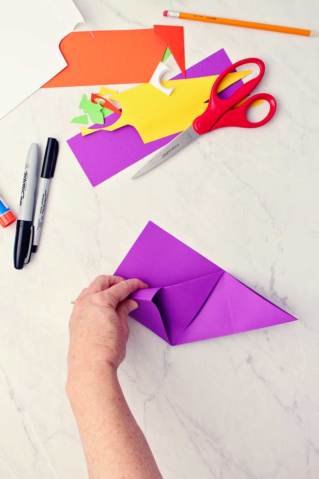 View of hand folding in the first corner of the purple paper to secure it into the diagonal center fold.