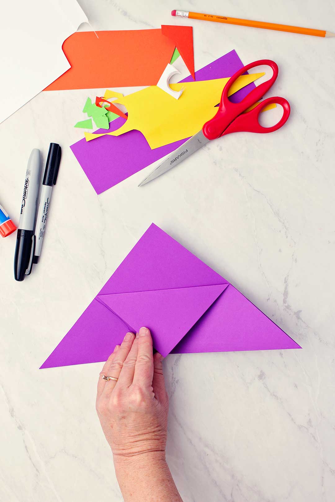 Hand showing center triangle fold coming from a larger folded triangle of purple paper.