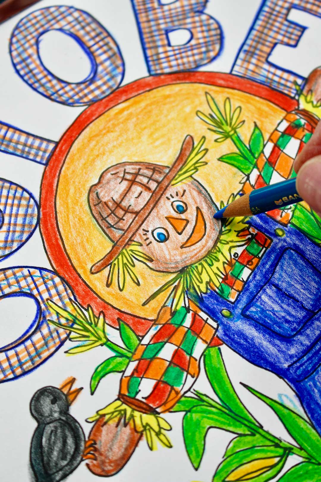 Blue colored pencil shading in detail in the scarecrows face of the October coloring page.