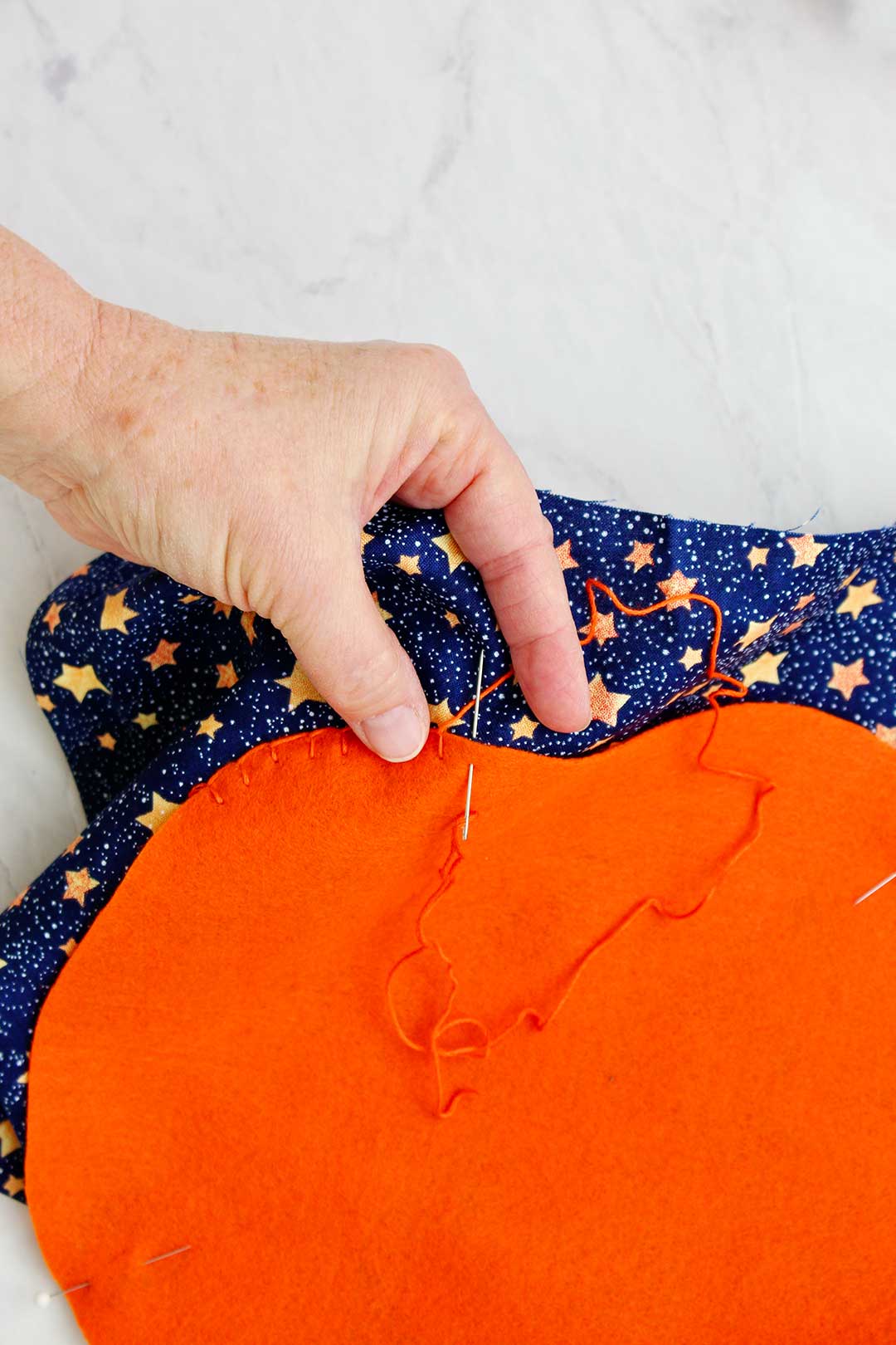 Hand sewing orange thread around felt pumpkin decoration.