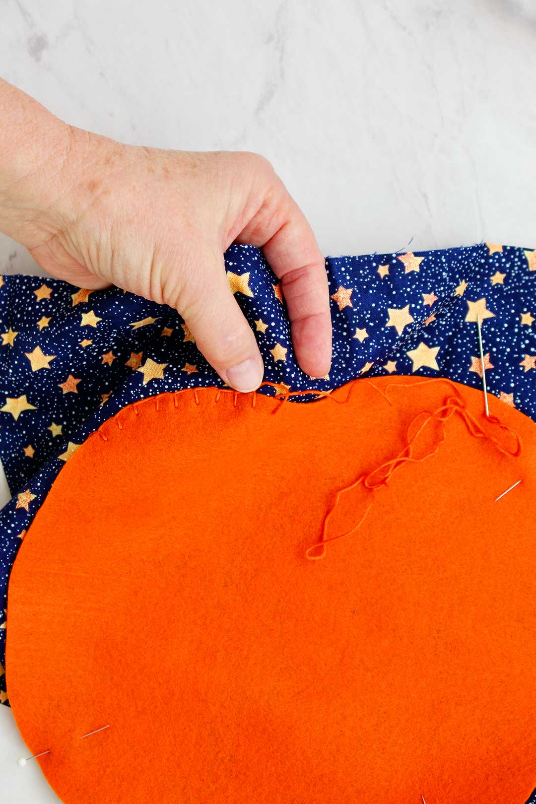 Hand sewing orange thread around the outline of the felt pumpkin decoration.