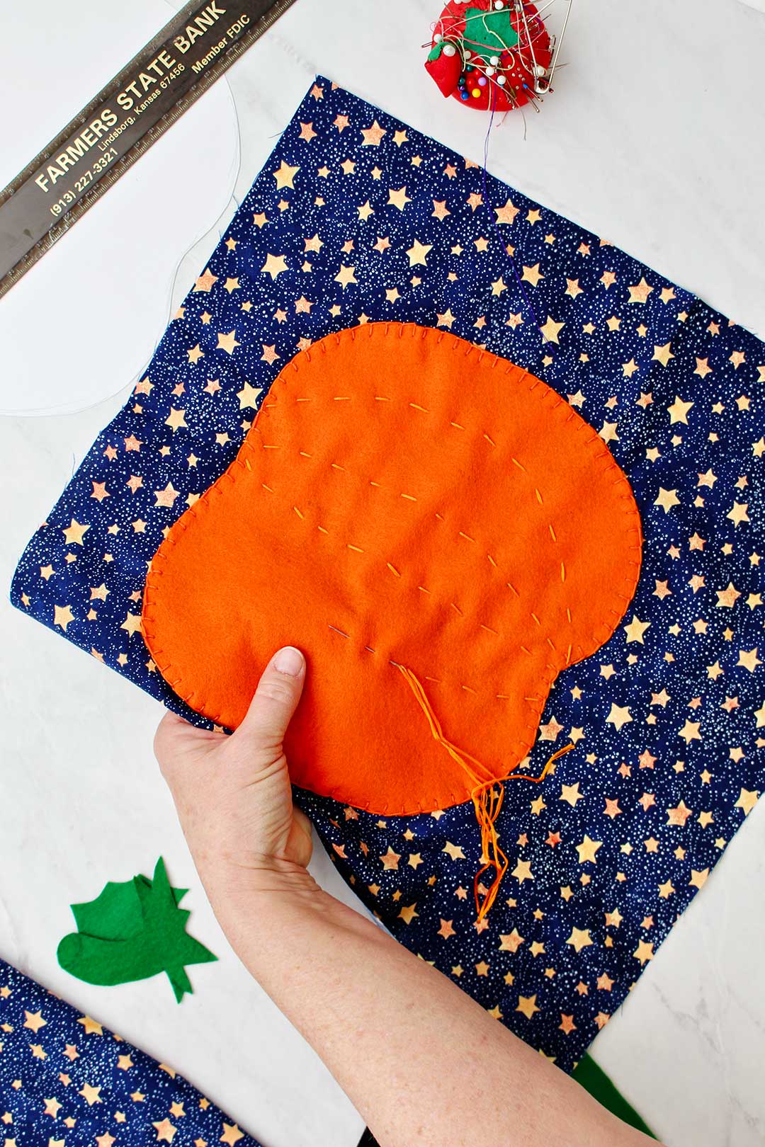 Hand holding pumpkin cutout on starry fabric while sewing.
