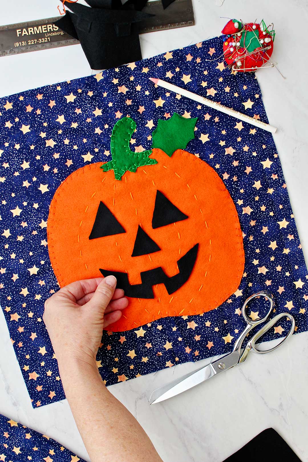 Hand placing the black felt cut out of a jack-o-lantern mouth on sewed pumpkin decoration for pillow.