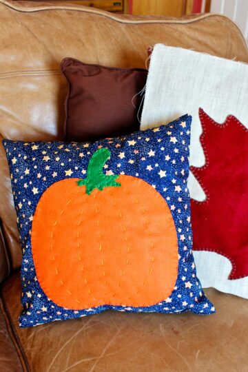 Two fall pillows resting on a tan leather couch.