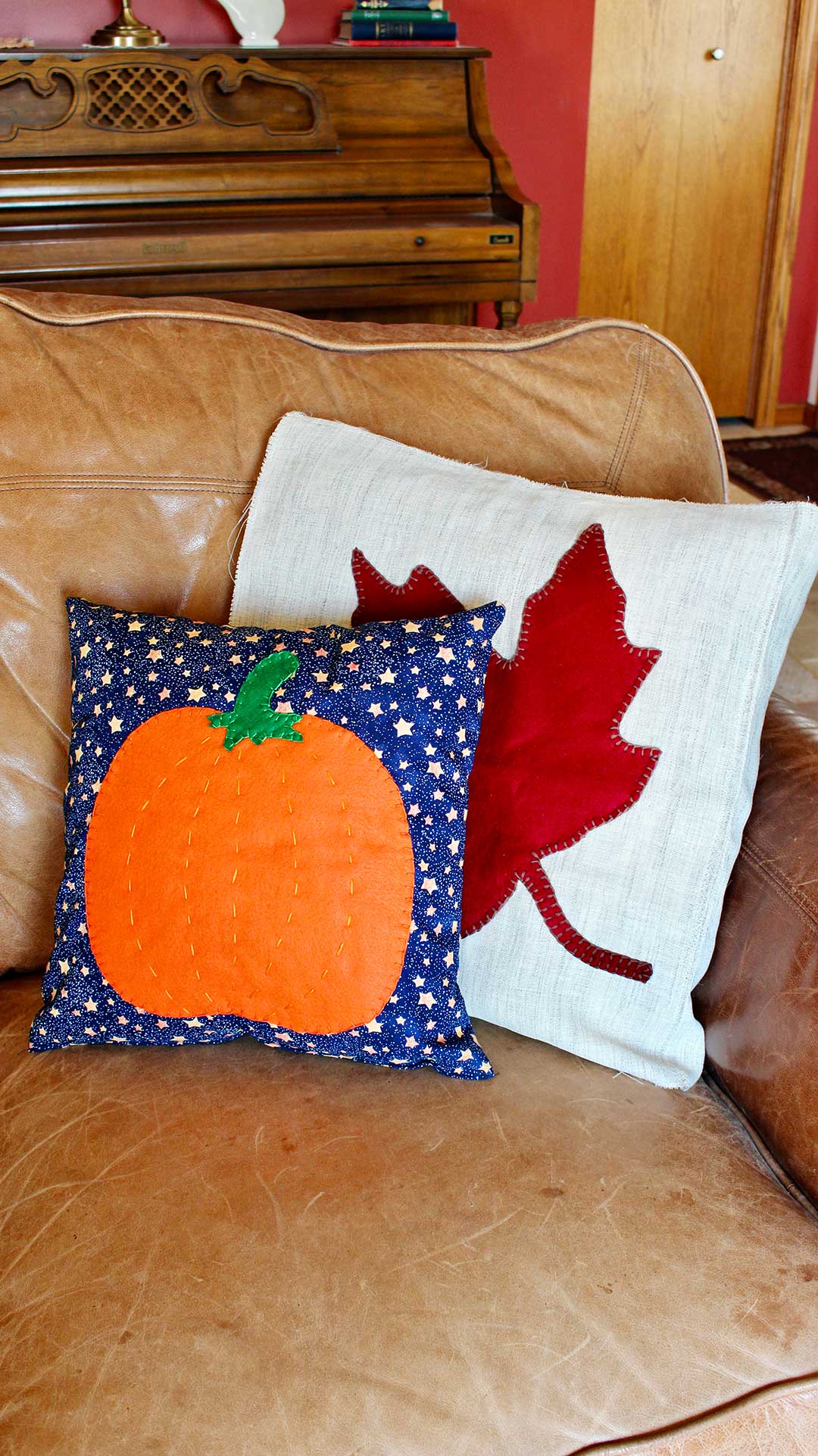Two completed fall pillows on a tan leather couch.