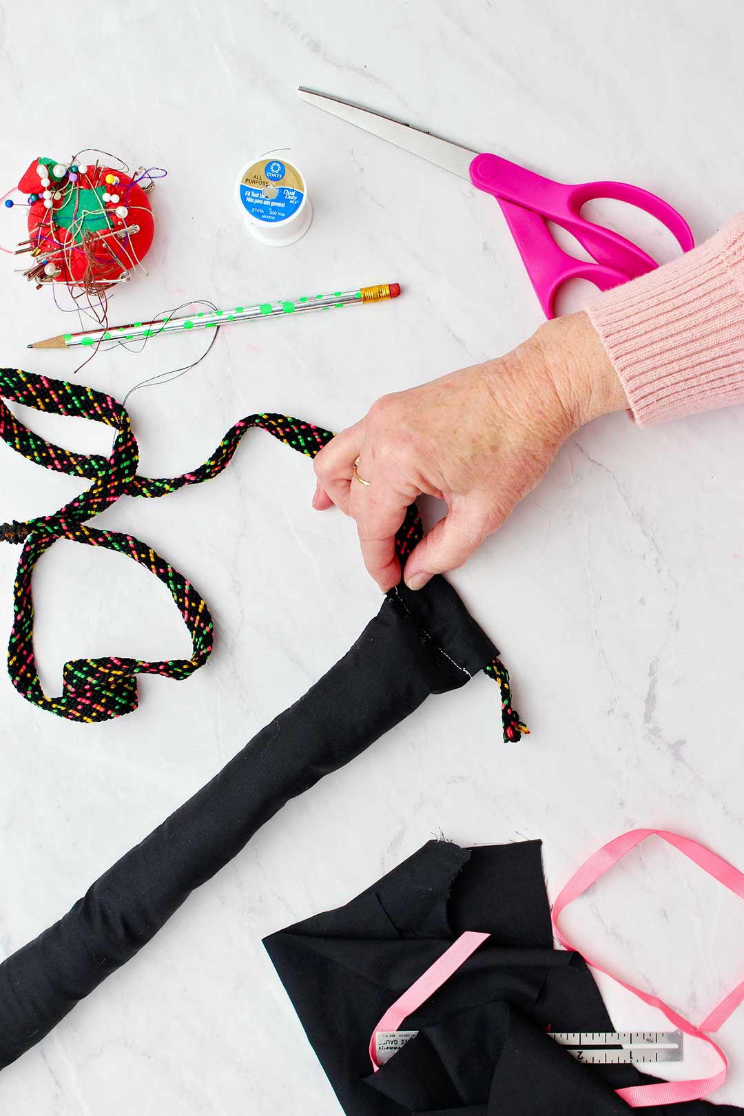 Hand threading colorful rope through a sewn loop in black cat tail for costume.