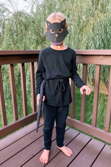 Young girl with blonde hair dressed up as a black cat on a deck.