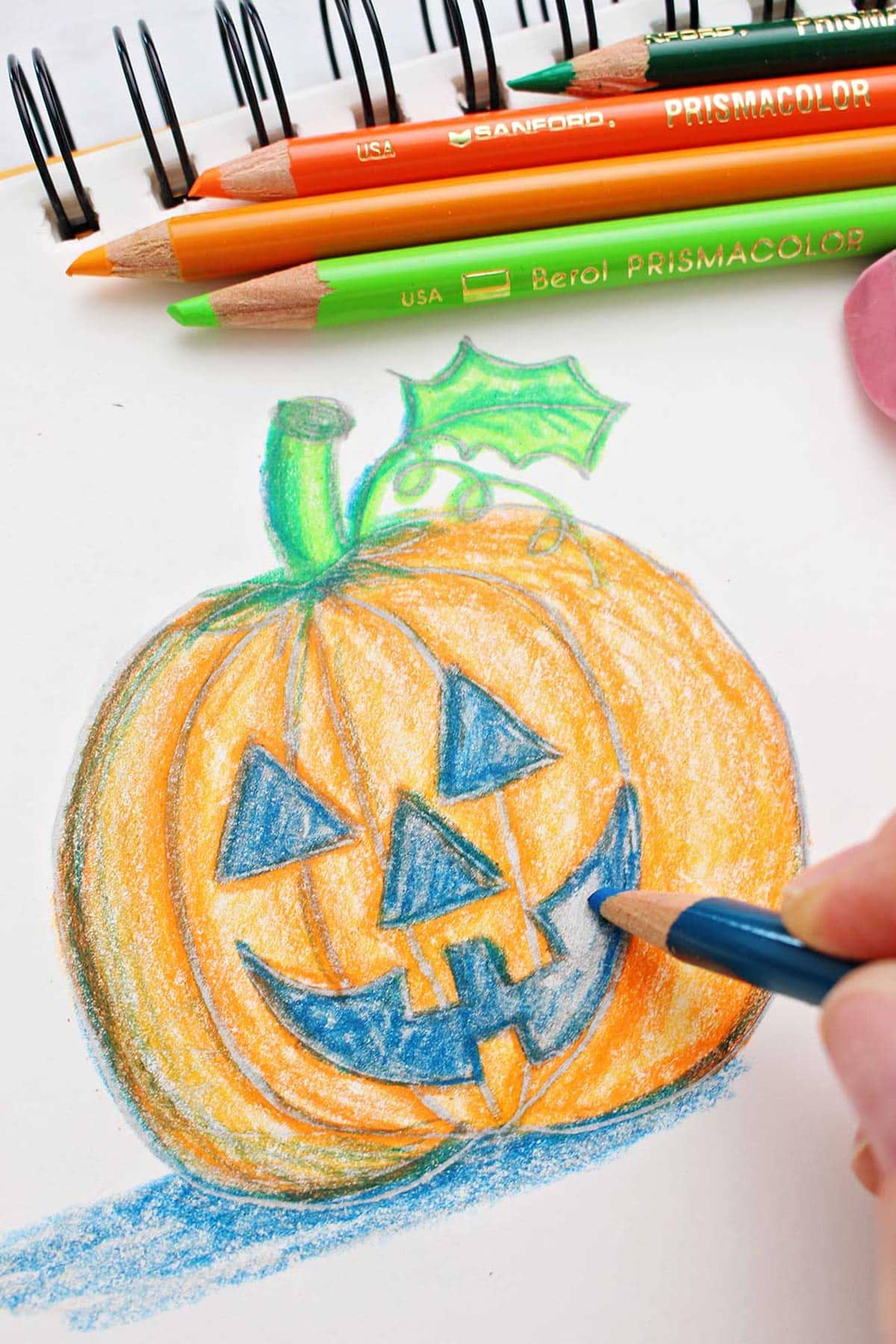 Hand filling in the mouth of a jack-o-lantern drawing with colored pencils.