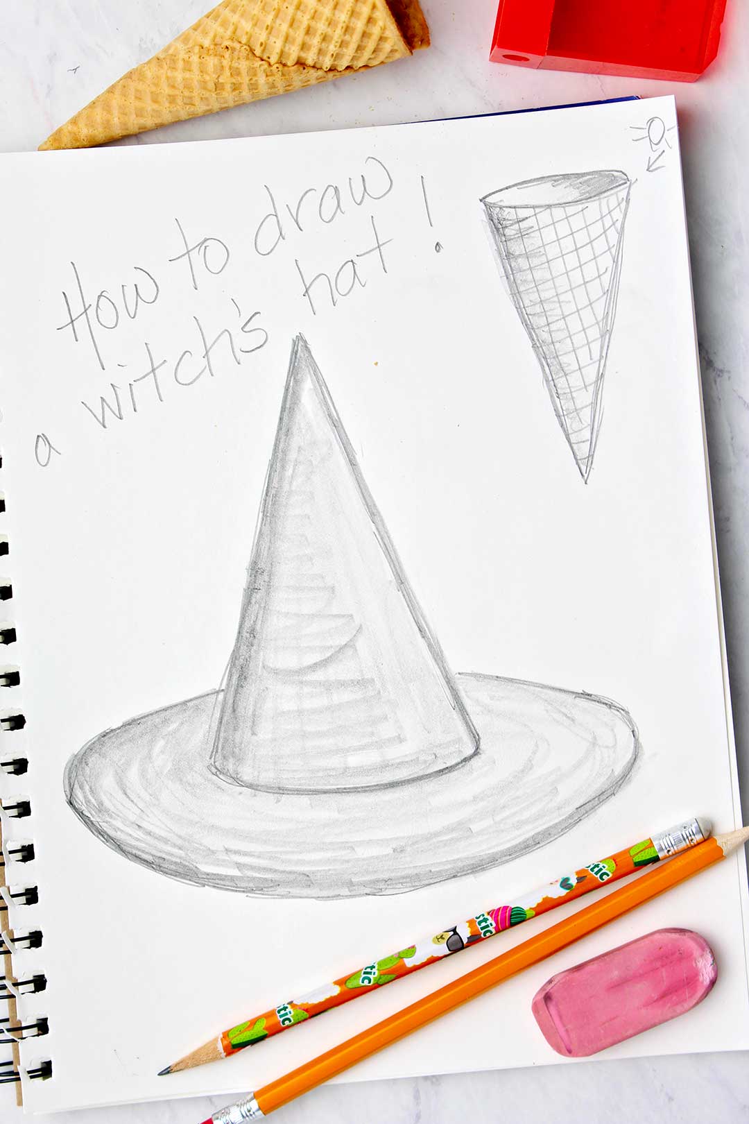 Final pencil drawing of a witches hat in a sketchbook. Two pencils, an eraser and an ice cream cone are also in the photo.