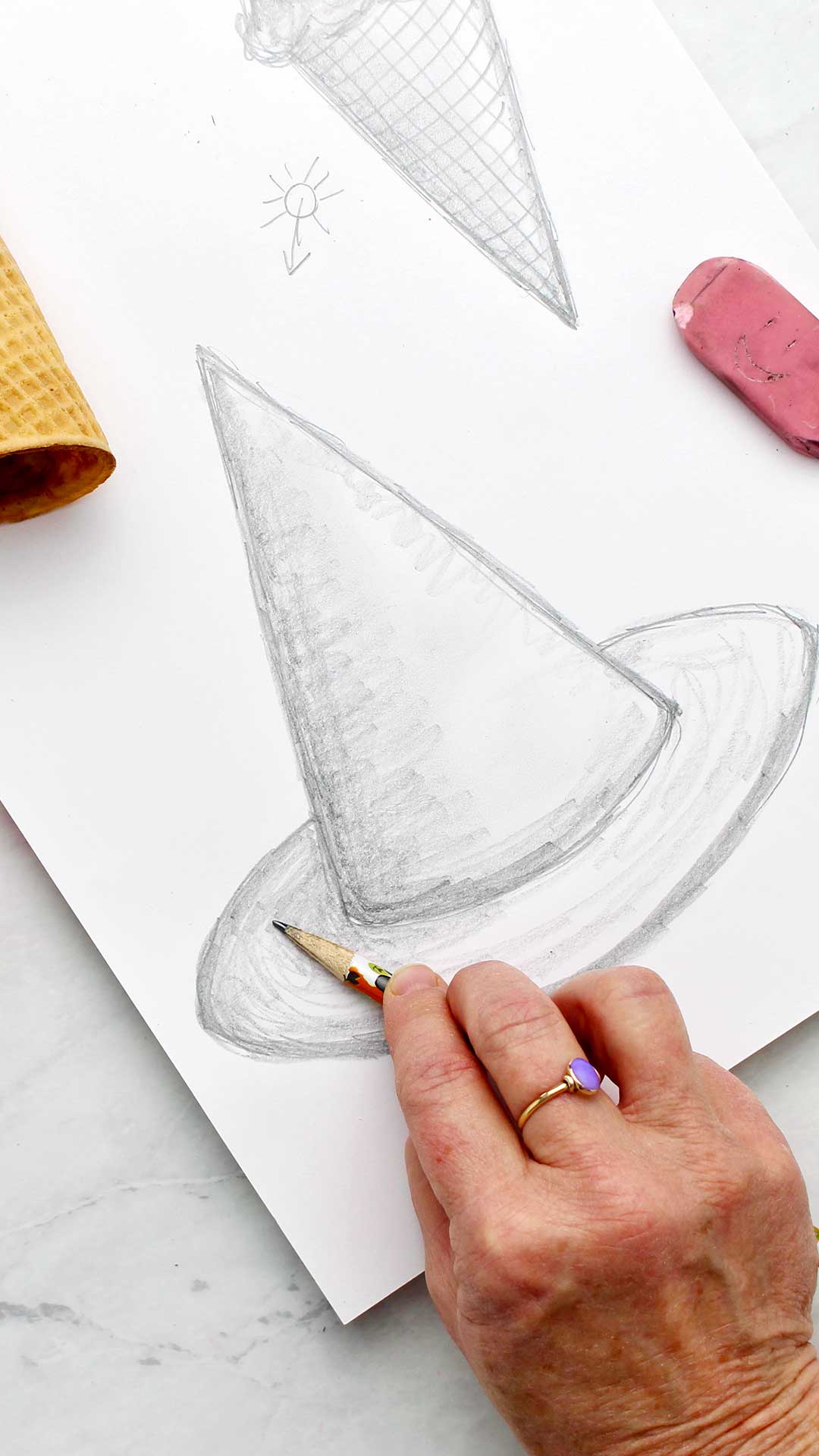 A hand shading with the side of a pencil on a drawing of a witches hat.