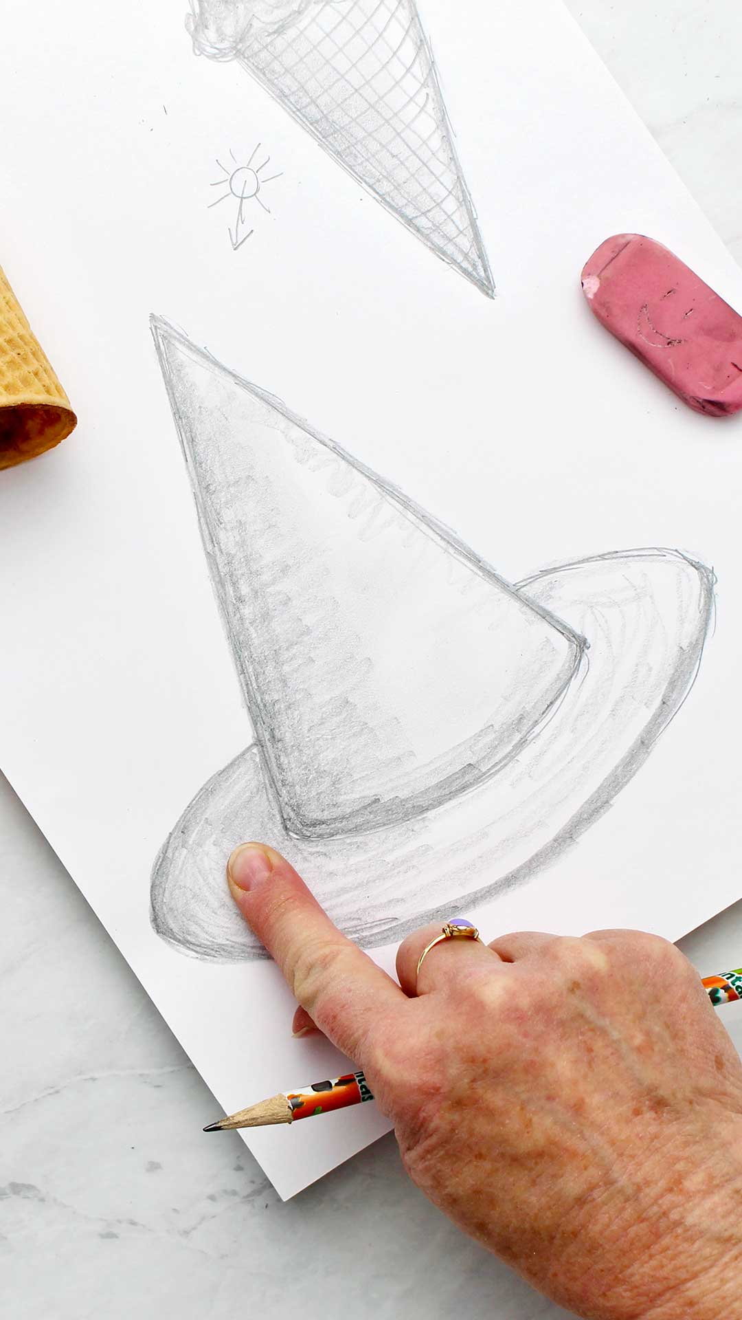 A finger blending the shading on a pencil drawing of a witches hat.