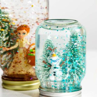 Two mason jar snow globes with trees and Olaf and Anna characters.