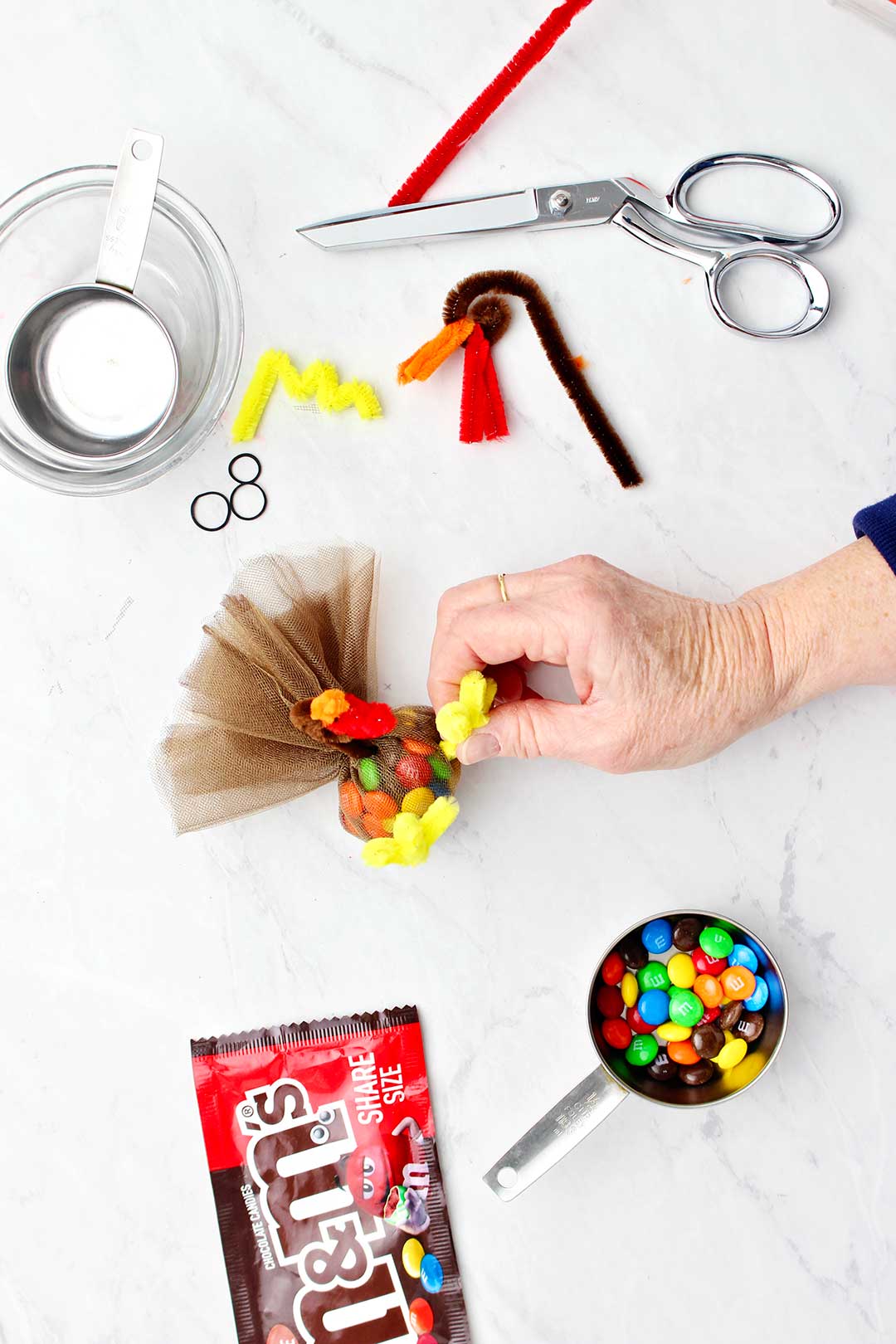 Hand securing pipe cleaner feet on turkey with various supplies near by.