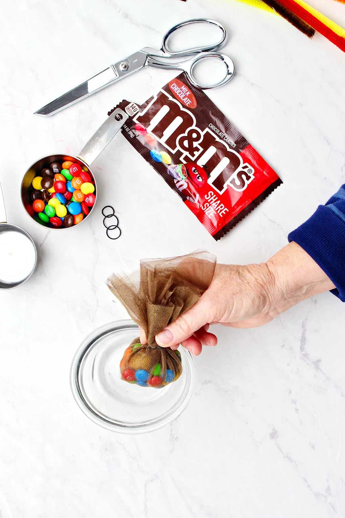 Hand holding bundle of brown tulle filled with m&ms.